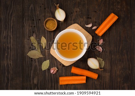 Traditional homemade beef bone broth with vegetable in white plate on dark rustic wooden background. Healthy low-calories collagen food concept. Top view, copy space.