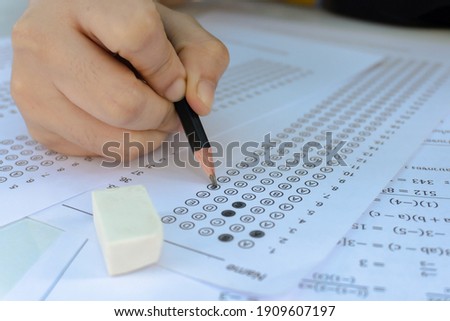 Students hand holding pencil writing selected choice on answer sheets and Mathematics question sheets. students testing doing examination. school exam Royalty-Free Stock Photo #1909607197