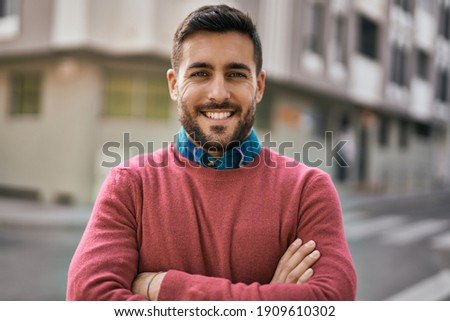 Young hispanic man with arms crossed smiling happy standing at the city.