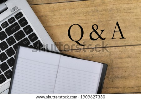 Selective focus image of laptop and book with Q n A wording on wooden background. Business concepts. 