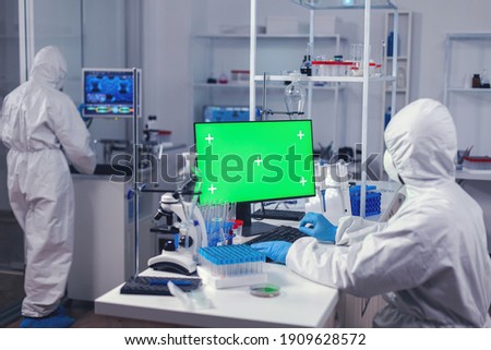 Laboratory technician in medicine lab uses computer with green screen dressed in ppe. Team of microbiologists doing vaccine research writing on device with chroma key, isolated, mockup display.