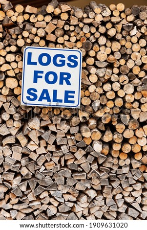 Closeup of a Stack of Firewood with a commercial sign with the short phrase, Logs For Sale, in English language.