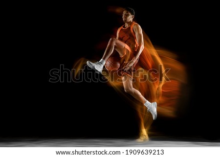 Flying. Young arabian muscular basketball player in action, motion isolated on black background in mixed light. Concept of sport, movement, energy and dynamic, healthy lifestyle. Training, practicing.