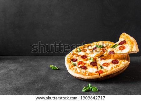 Traditional Italian Pizza with mozzarella, tomatoes and salami over black background, copy space. Delivery pizza or pizzeria promotional concept.
