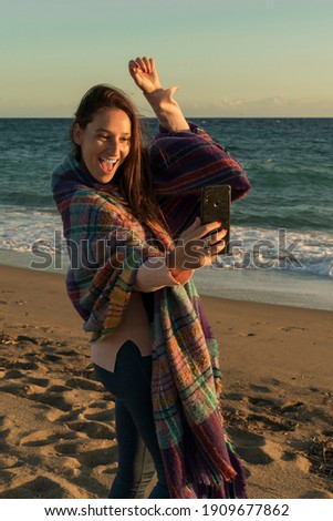 Smiling woman wearing blanket taking selfie on the beach