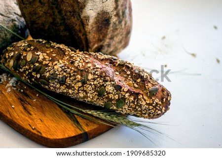 Homemade multigrain bread with fenugreek, flax, pumpkin, sesame seeds in assortment on a wooden board against a background of wheat ears