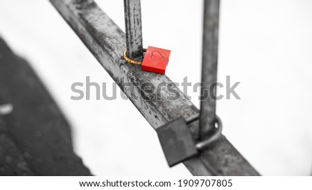 Heart engraved on red wedding padlock hanging on bridge railing. Monochrome background.