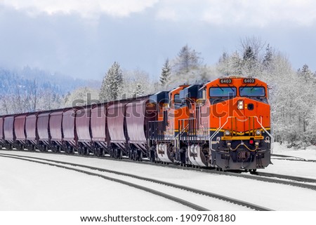 Winter scene of a locomotive pulling freight cars close to Whitefish, Montana with exhaust poring out of the engine on a cold day in January
