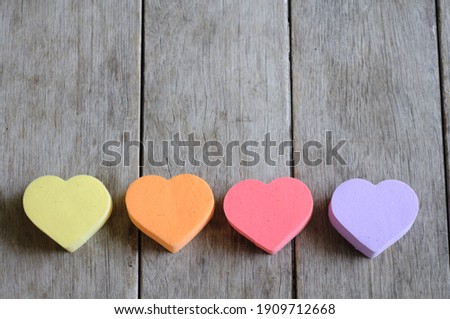 Four heart-shaped sponges are placed on the wooden floor.  There are yellow, orange, pink and purple.  Taken from natural light  There is a blank space for placing text on top of the image.
