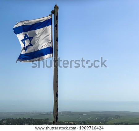 Partially torn israeli flag is waving in the wind against blue sky background