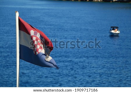 Flag of Croatia, blowing in the wind. Adriatic sea, island and boats in the background. Selective focus.