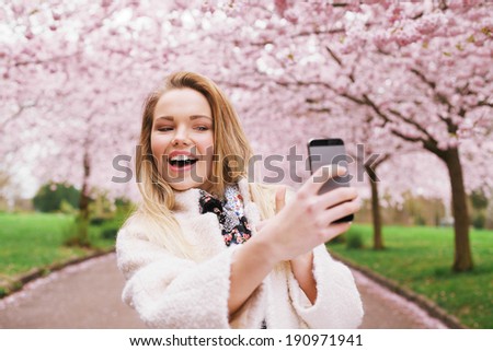 Happy young woman photographing herself using her mobile phone. Caucasian female talking selfie with her smart phone at park.