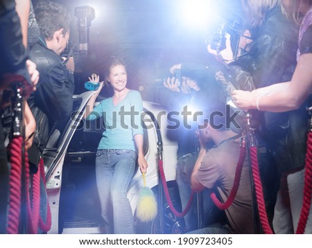 Excited woman with cleaning equipment getting out of limousine in front of paparazzi