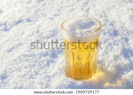 A glass on the snow on a sunny day is filled with foaming beer