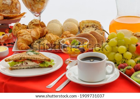 Gastronomy. Breakfast table with cup of coffee, sandwich, fruits, juice jar, fruits and various breads with red tablecloth.