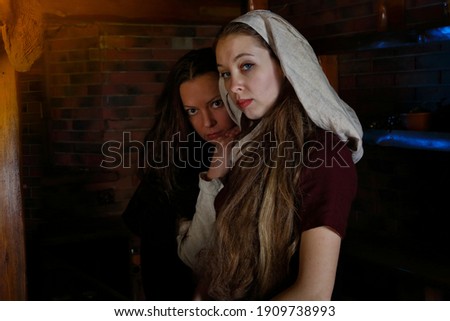 Women in historical costumes. Portraits of two maids in a tavern. A scene from medieval life. Historical reconstruction of a restaurant lunch. Girls in vintage dresses and  old headscarf. Renaissance Royalty-Free Stock Photo #1909738993