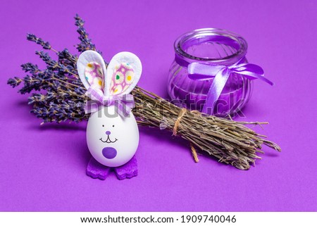 Monochromatic lavender Easter concept. Fragrant flowers, natural purple candle and cute bunny. Matte lilac background, place for text