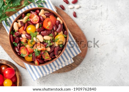 Salad of white and red beans, tomatoes and herbs in a ceramic bowl on a gray concrete table.. Tasty vegan food. Copy space for text Royalty-Free Stock Photo #1909762840