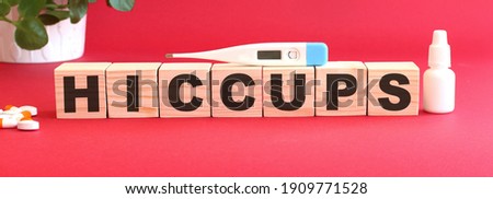 The word HICCUPS is made of wooden cubes on a red background with medical drugs.