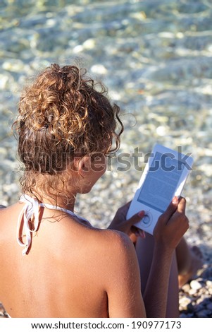 Beautiful woman reading ebook on the beach 
