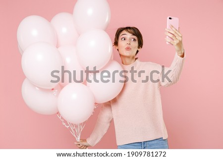 Pretty young woman 20s in casual sweater celebrating hold air balloons doing selfie shot on mobile phone blowing lips isolated on pastel pink background. Birthday holiday party people emotions concept