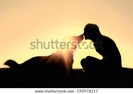 a silhouette of a happy young woman is sitting outside at sunset lovingly kissing her large German Shepherd mix breed dog. Royalty-Free Stock Photo #190978217