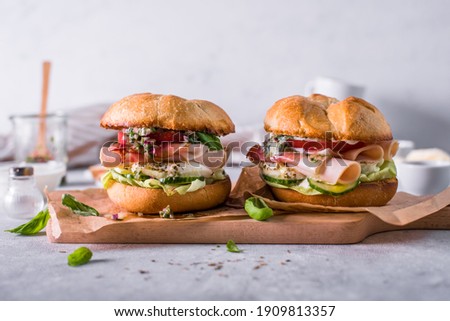 
Caprese burgers. Sandwiches with mozzarella cheese, tomato, cucumber, and ham. Given on paper on a board. Light background