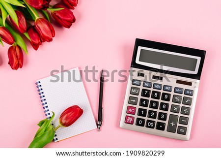 Bouquet of red tulips on pink paper background with calculator, spiral notebook and pen are a template for advertising or visualization of blog with copy space for text. Business holiday. Certificate.