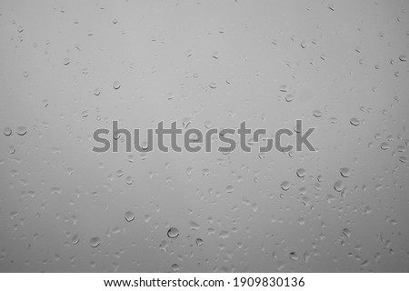 Textured water drips on white glass - background. Water belongs through a glass window. Close up of water droplets on glass. After a summer shower, heavy rain belongs on the window pane. Condensation