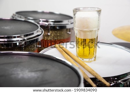 Glass of light beer on professional drum set closeup. Drumsticks, drums and cymbals, at live music rock concert, in the club stage, bar, or in recording studio.  White background.