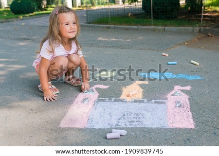 Girl drawing castle with colored chalks on the sidewalk near the house on sunny summer day. Kids painting outside. Creative development of children. Royalty-Free Stock Photo #1909839745
