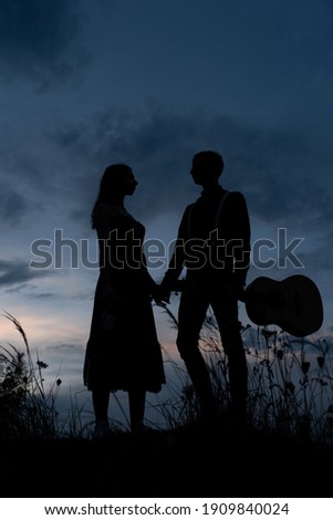 Silhouette of a couple in love on a date. The man holds the girl's hand. The guy in crabs has a guitar. Filmed at sunset.