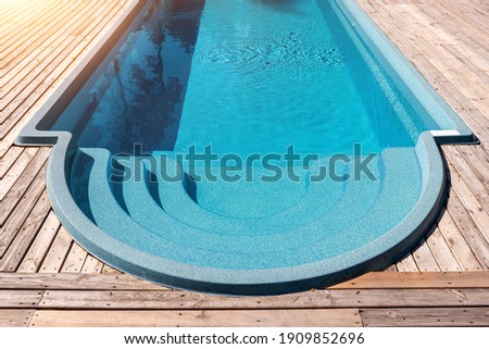 New modern fiberglass plastic swimming pool entrance step with clean fresh refreshing blue water on bright hot summer day at yard or resort hotel spa area. Wooden flooring deck of teak or larch board Royalty-Free Stock Photo #1909852696