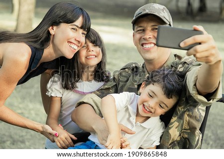 Joyful happy disabled military man taking selfie with his wife and two kids in park. Family togetherness and support concept