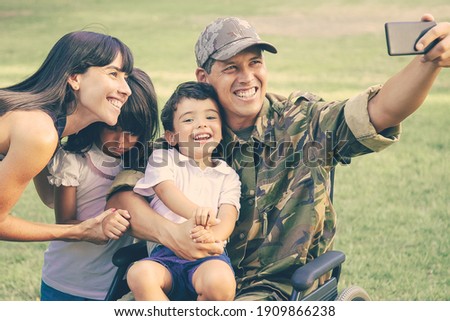 Happy disabled military man taking selfie with his wife and two kids in park. Veteran of war or leisure time with family concept