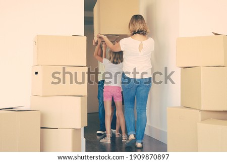 Family couple and two girls leaving apartment, carrying cartoon box together. Back view. Relocation concept