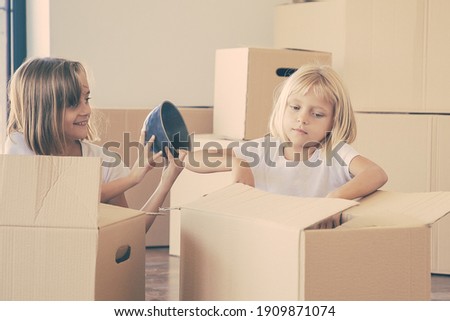 Kids unpacking things in new apartment, sitting on floor and taking objects from open cartoon boxes. Relocation or moving concept