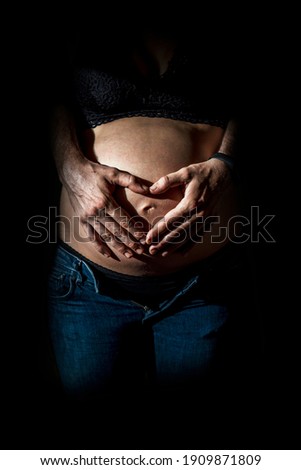 Portrait of young pregnant couple smiling happy putting their hands together in a heart shape on top of their belly
