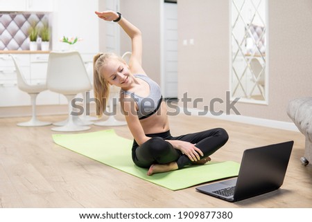 young attractive girl is engaged in fitness at home and looks at the laptop. quarantine fitness concept
