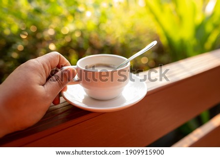Hand holding coffee cup on green nature bokeh background on morning, caffeine beverage for fresh lifestyle, close up cup and steam water on light of sunny wallpaper, beautiful photo for graphic idea
