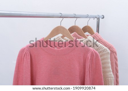 Three warm different sweaters hanging on rack against gray background,
