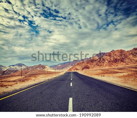 Vintage retro effect filtered hipster style travel image of Travel forward concept background - road in Himalayas with mountains and dramatic clouds. Ladakh, Jammu and Kashmir, India