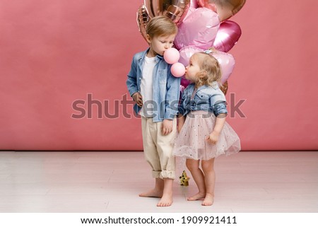 Little boy and girl hugging, dancing, smiling and having fun near big branch of pink heart-shaped ballons. Valentin’s day concept . Isolated on pink background.