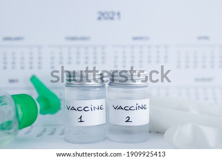 covid-19 vaccine and immunisation against the pandemic, ampoules with Vaccine 1 and Vaccine 2 labels side by side next to 2021 yearly calendar and mask gloves and sanitizer