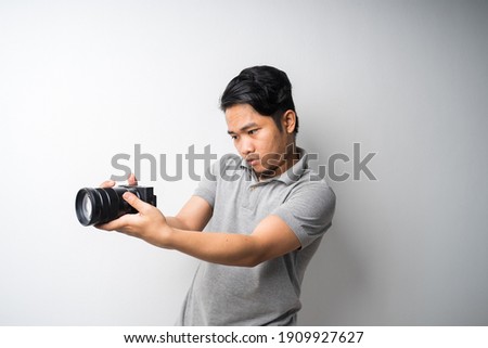 Young Asian man face expression with dslr or mirrorless camera. Photography, creative industry. Isolated selective focus.