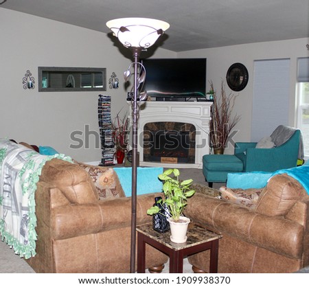 Still life interior. Picture of a living area in with a tv, white fireplace, teal accents, light brown leather furniture , dvd stand gray mirror, lamp, green plant, clock with a farmhouse look.
