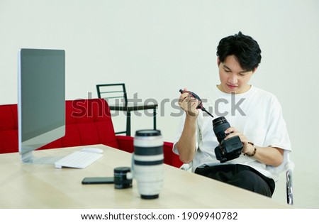 Professional photographer Asian man sitting and cleaning camera and accessories after working and shooting model at desk in front of computer laptop in studio. Photography picture image concept.