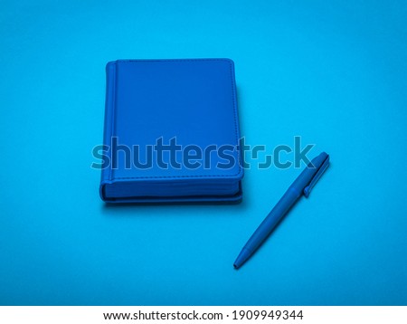 Blue pen and blue notepad on a blue background. Monochrome image of office accessories.