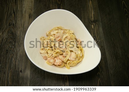 A white bowl with fettuccine alfredo noodles with shrimp.