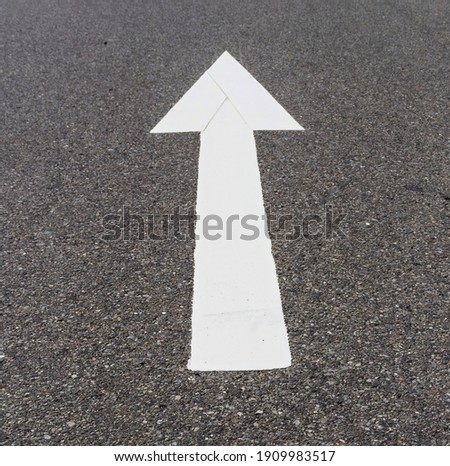 White arrow on black asphalt points in a forward direction, to guide traffic in a safe manner into a parking space.